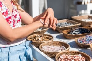 Young woman shopping for colorful stone beach bead bracelets trying on jewelry in outdoor market shop store in European, Greece, Italy or Mediterranean town village in summer
