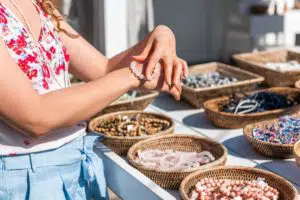 Young woman shopping for colorful stone beach bead bracelets trying on jewelry in outdoor market shop store in European, Greece, Italy or Mediterranean town village in summer Young woman shopping for colorful stone beach bead bracelets trying on jewelry in outdoor market shop store in European, Greece, Italy or Mediterranean town village in summer